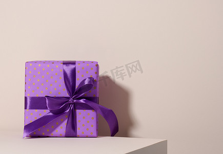 用喜庆的紫色纸包装的盒子，用丝带绑在米色背景上，生日礼物，惊喜