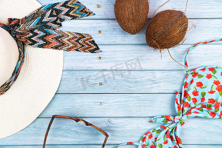蓝色木质背景上，可以看到戴着眼镜、泳衣和椰子的草白帽子的顶视图。暑假概念