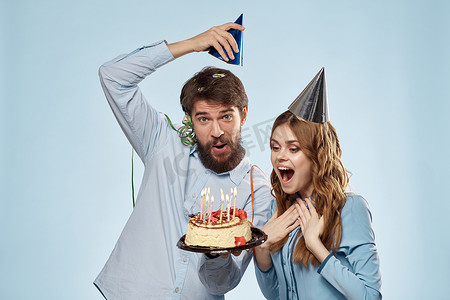 吹蛋糕蜡烛摄影照片_快乐的男人和女人吹灭蛋糕蜡烛假日装饰蓝色背景