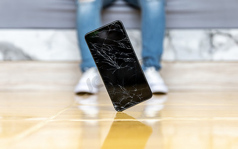 人们将智能手机摔在地板上破碎的屏幕上