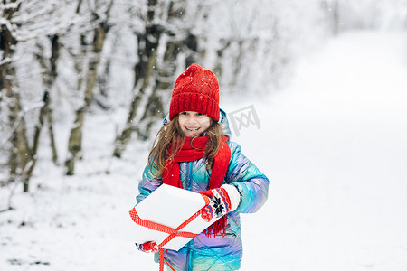圣诞围巾摄影照片_圣诞节前夕，冬天户外带着圣诞盒礼物的小女孩。