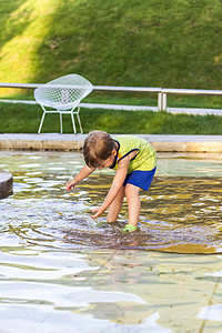公园里的一个孩子正在喷泉里湿脚，他很高兴。