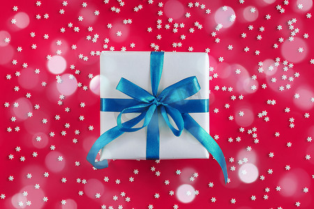 用白纸包裹的礼盒，在喜庆的深红色背景上带有蓝色蝴蝶结，上面有许多雪花