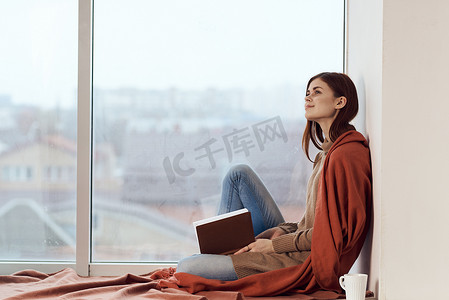 窗边拿着一本书和一杯咖啡的女人