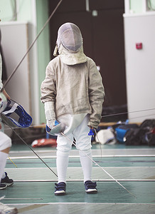 击剑比赛中穿着白色衣服和防护面具的击剑比赛的年轻参赛者