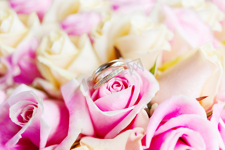金色婚礼装饰摄影照片_新娘花束上的金色结婚戒指与粉红色和黄色的玫瑰。