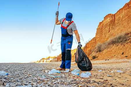 男子志愿者用伸手杖在海滩上收集垃圾