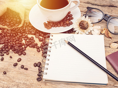 热咖啡杯加咖啡豆和笔记本用木制的桌子上的铅笔。