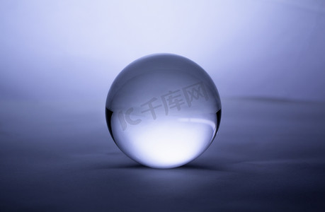 蓝色渐变背景摄影照片_蓝色渐变背景上透明的水晶玻璃球球体。
