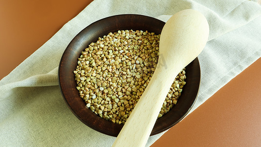 棕色粘土盘和木勺中的生绿色荞麦。