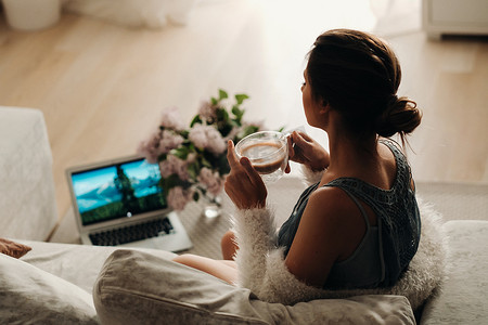 一个轻松的女孩在家喝咖啡看电影。国内平静。女孩舒适地坐在沙发上喝咖啡