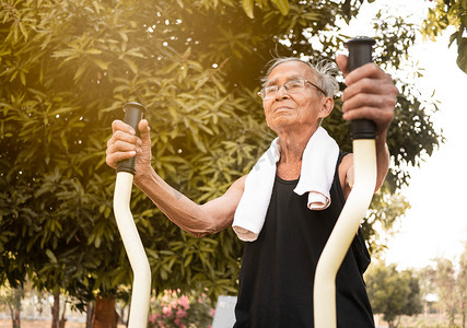 阳光明媚的日子里，穿着运动服的亚洲老人在公园的户外健身器材上锻炼身体。