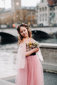 一个穿着粉色公主裙、手里拿着花束的小女孩走过苏黎世老城。瑞士城市街道上一个穿着粉色裙子的女孩的肖像