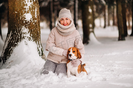 一个冬天的女人和她的宠物狗比格犬在冬季森林里玩耍