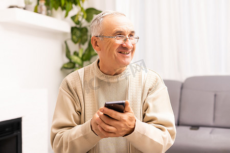 技术、人、生活方式和沟通概念 — 快乐的老人在家里拨打电话号码并在智能手机上发短信。