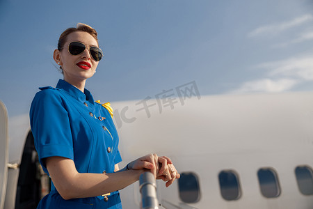 白天，身着蓝色制服、戴着太阳镜、站在楼梯上的漂亮空姐的肖像