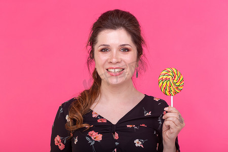 棒棒糖粉色背景摄影照片_糖果、对甜食的成瘾和情感概念 — 粉色背景中拿着棒棒糖的快乐女人
