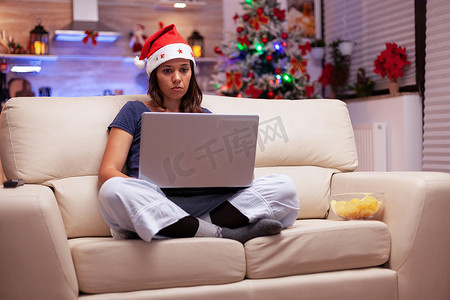坐在沙发上的莲花位置上，在笔记本电脑上写商务电子邮件的女性