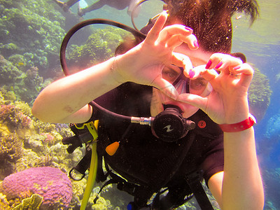 埃及沙姆沙伊赫，可爱的女潜水员用手势表达爱意，与搭档教练一起在有珊瑚礁的红海水下安全游泳
