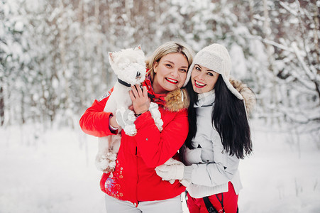 牵狗摄影照片_两个女孩和一只狗在寒冷的冬季森林里的肖像。