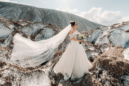 美丽的新娘穿着婚纱，在盐山顶上放着花束。