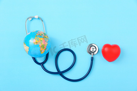心脏蓝色背景摄影照片_世界卫生日概念、听诊器、地球和红色心脏