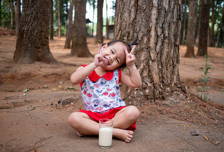 亚洲小孩在花园里喝着玻璃杯里的牛奶，味道鲜美。