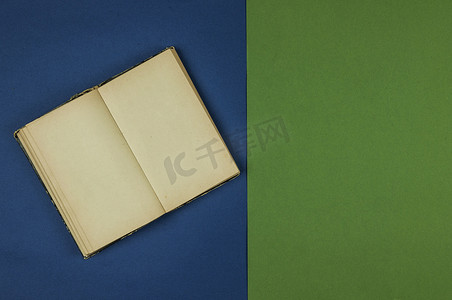 黄色页摄影照片_带有空白页的旧打开书躺在绿色和蓝色背景上。