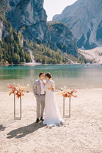 牡丹被罩摄影照片_新娘和新郎站在仪式现场，以意大利布拉伊埃斯湖为背景，以秋花柱拱门为背景。