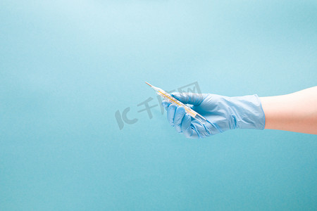 体温计摄影照片_蓝色一次性医用手套中的女手握着水银温度计，蓝色背景复制空间