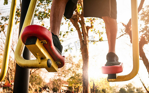 在阳光明媚的日子里，穿着运动服的亚洲老人在公共公园的户外健身器材上锻炼身体以保持健康。