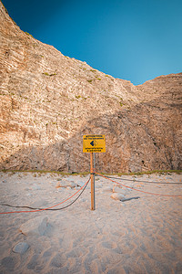 悬崖附近一根带绳索的杆子上没有非法侵入标志，警告落石，希腊扎金索斯海滩 Navagio 附近的海难。