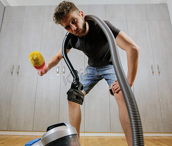 整理客厅摄影照片_一个拿着除尘刷和吸尘器的男人。