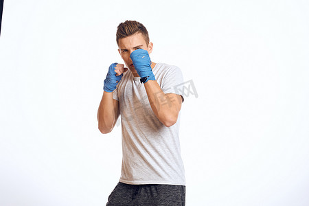 戴着蓝色手套的运动男拳击手在浅色背景裁剪视图中练习拳击