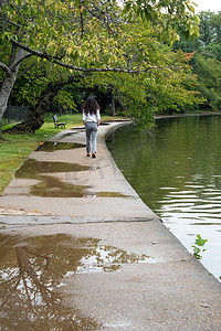 男士长发摄影照片_一名男子走开小路上的水坑，池塘反射着树木