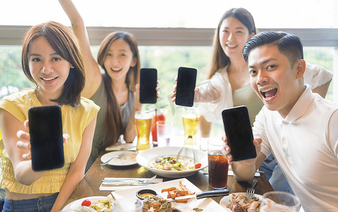 快乐的年轻群体在餐厅里展示带空白屏幕的手机