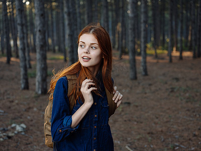 红发摄影照片_红发赤裸上身的女人，背着背包，在松树林里休息，视野开阔