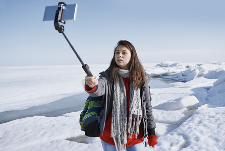 独脚架摄影照片_女旅行者在冰冷的户外使用独脚架拍摄自拍图片