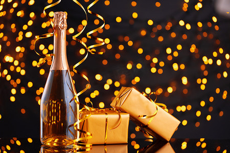 饮料瓶摄影照片_圣诞灯光模糊背景下的香槟瓶和包装礼物