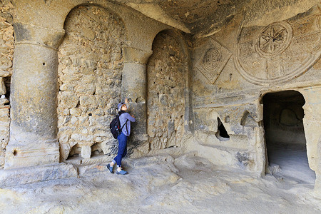 一位年轻女子正在检查旧地下教堂的圆柱大厅的内部，该圆柱大厅雕刻在砂岩悬崖上。