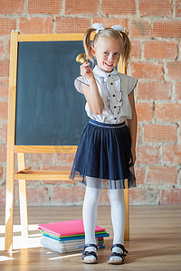穿着校服的可爱小女孩在学校董事会旁边摆着铃