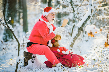 圣诞老人在白雪皑皑的森林里户外阅读圣诞愿望清单。
