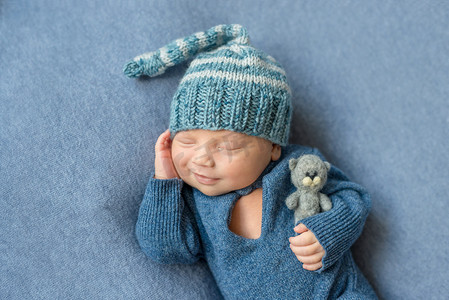 穿着蓝色西装、戴着玩具帽子的微笑睡着的新生儿