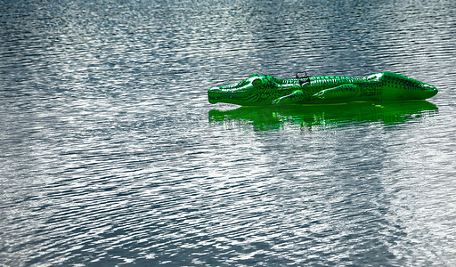 游动摄影照片_橡胶中的绿色鳄鱼在湖上孤独地游动