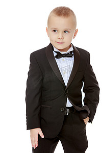 黑色西装白色衬衫摄影照片_穿着黑色西装打领带的时髦小男孩。