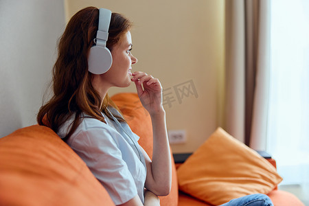 橙色沙发公寓里戴着耳机听音乐的美女
