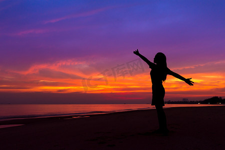 日落时站在海滩上举手的妇女剪影