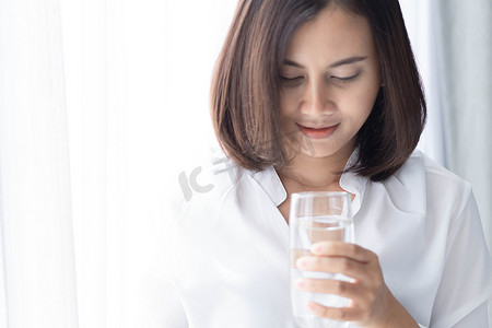 纯净水摄影照片_特写女人从玻璃杯中喝纯净水，玻璃中有光