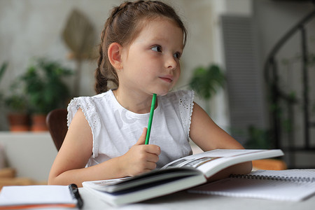 小女孩坐在家里的书桌旁做作业、自学材料、看书。