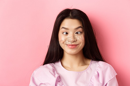 滑稽的亚洲女性的特写肖像，眯着眼睛，做着傻脸，站在粉红色的背景下